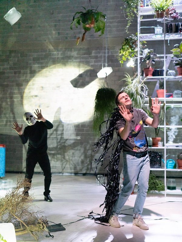 Zwei Performer auf einer Bühne, im Hintergrund volle Regale