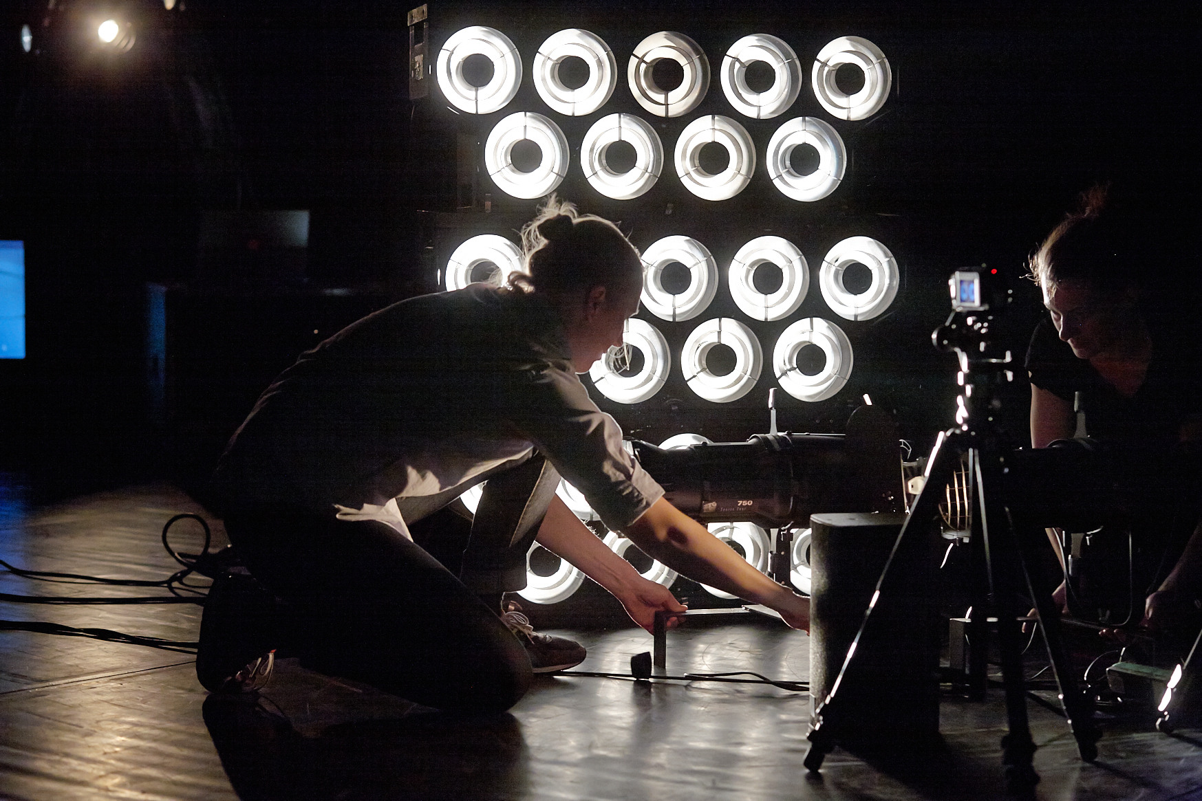 Zwei Bühnenarbeiterinnen kleben etwas auf dem Boden der Bühne ab