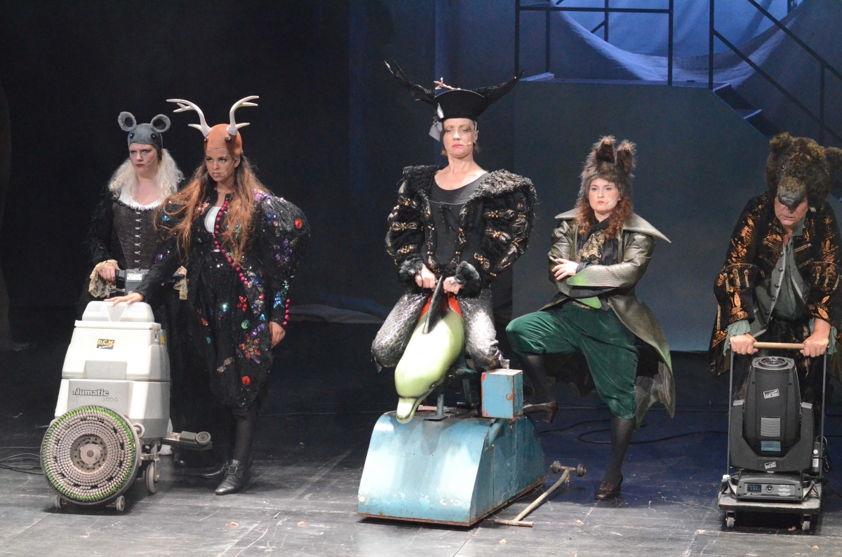 Szenenbild einer Oper in dem Menschen auf Spielgeräten sitzen