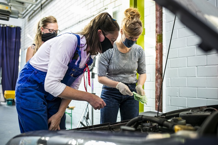 Drei Frauen blicken auf eine geöffnete Motorhaube
